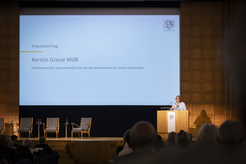 Eine Frau steht an einem Rednerpult. Auf der Leinwand hinter ihr wird ihr Name eingeblendet: Kerstin Griese (MdB), Parlamentarische Staatssekretärin bei der Bundesministerin für Arbeit und Soziales: 