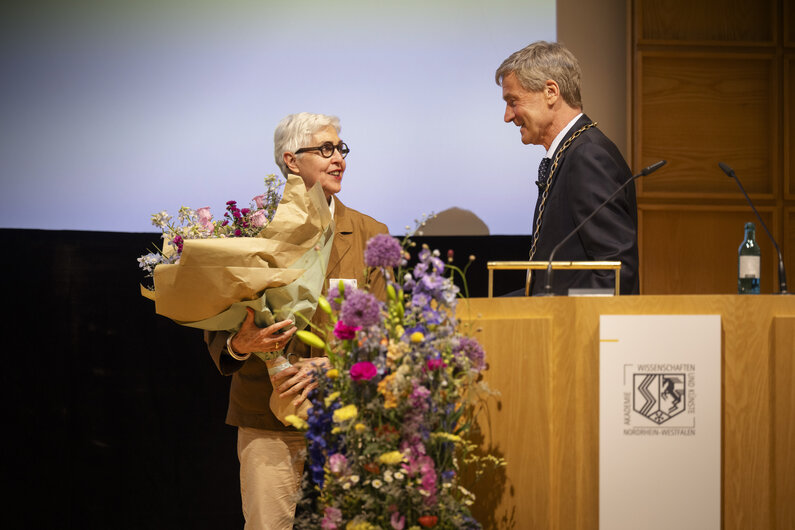 Ein Mann und eine Frau stehen auf einer Bühne. Die Frau hält einen Blumenstrauß in den Händen.
