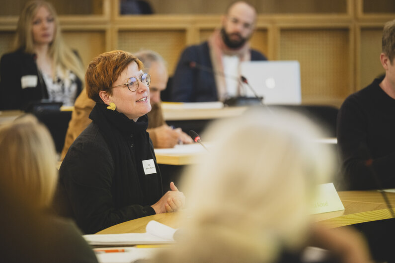 Eine Frau sitzt an einem Tisch. Sie spricht in ein Mikrofon.