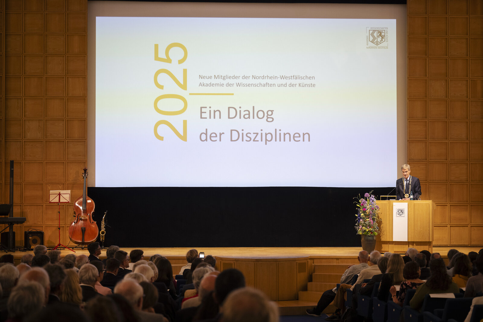 Ein Mann steht an einem Rednerpult. Im Hintergrund ist der Titel der Veranstaltung eingeblendet.