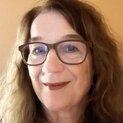 Eine Frau mit Brille schaut lächelnd in die Kamera. Sie trägt eine silberne Halskette.