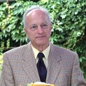 Ein Mann steht vor Sträuchern. Er lächelt und schaut nach halbrechts.