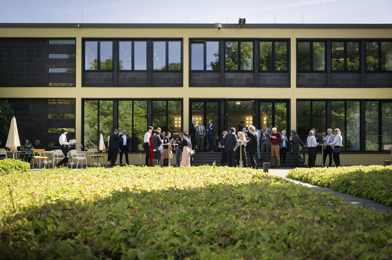 Im Garten der Akademie stehen Menschen an Stehtischen.