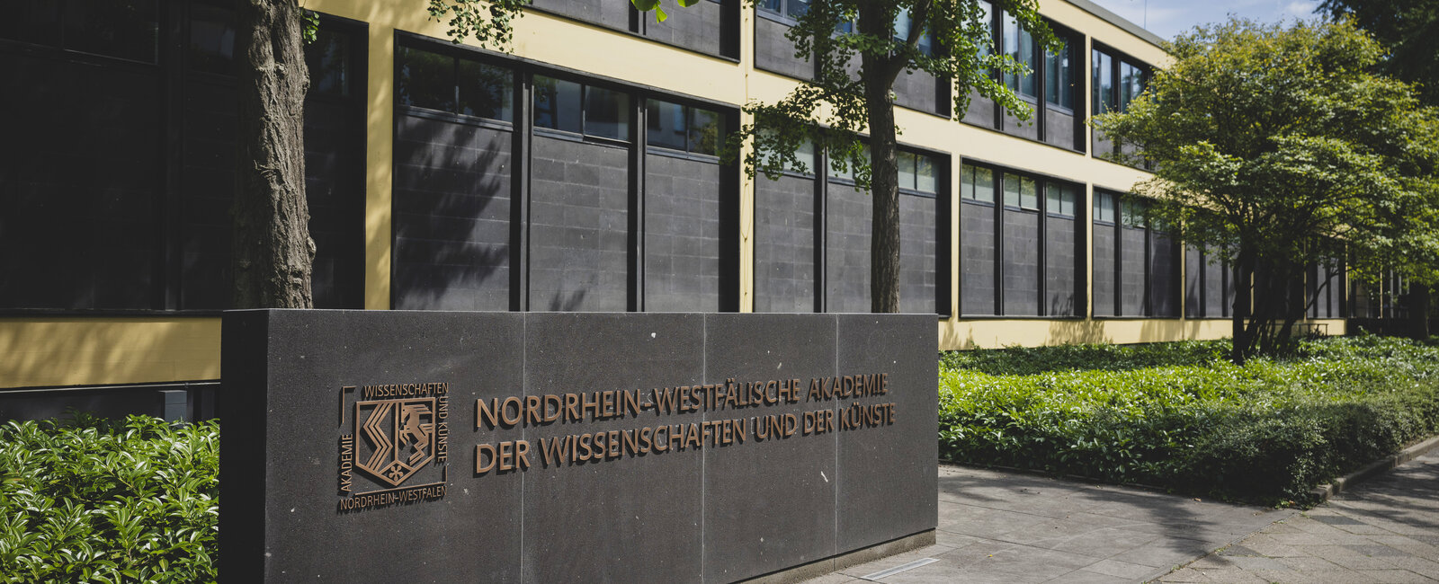Tafel mit Aufschrift "Nordrhein-Westfälische Akademie der Wissenschaften und der Künste" vor einem Gebäude