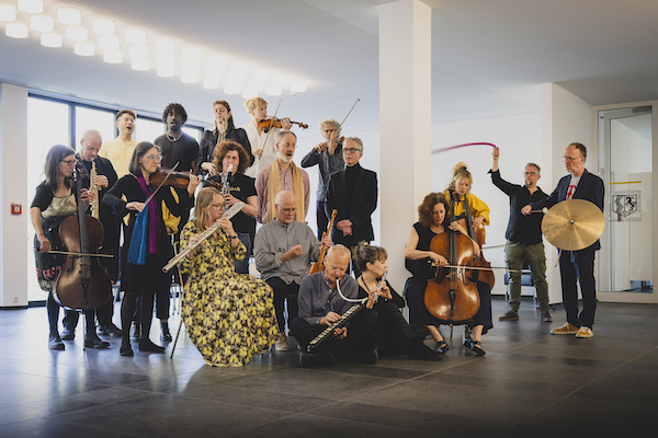 Im Foyer der Akademie haben sich Musikerinnen und Musiker aufgestellt. Sie spielen unterschiedliche Instrumente. 